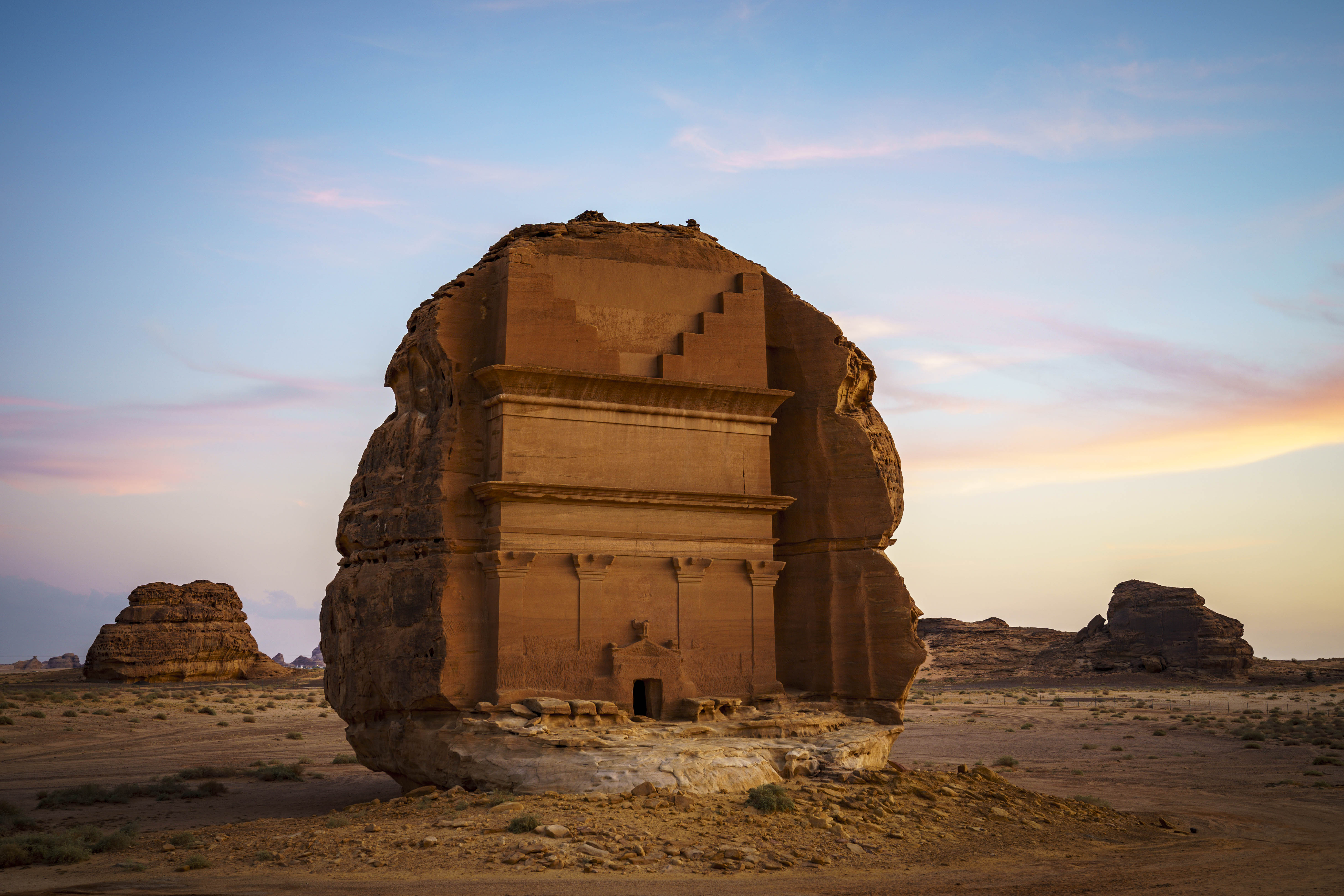 A stone building in the desert with Mada'in Saleh in the background Description automatically generated