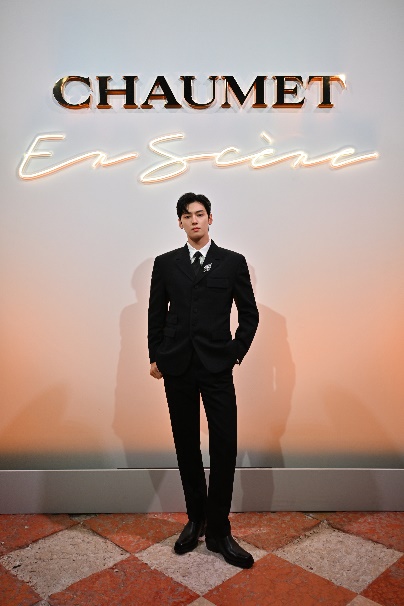 A person in a suit standing in front of a signDescription automatically generated