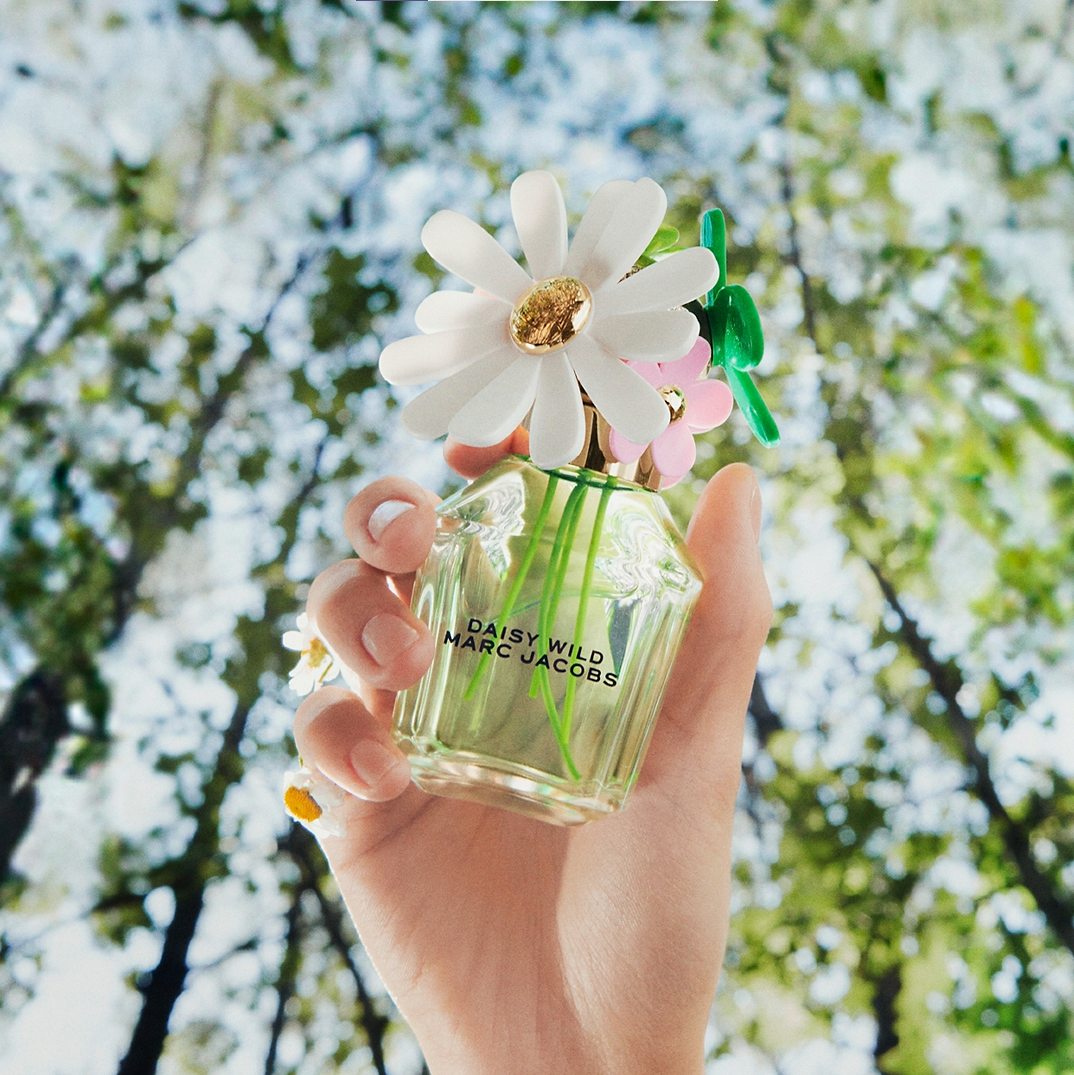 A hand holding a bottle of perfume with flowers Description automatically generated