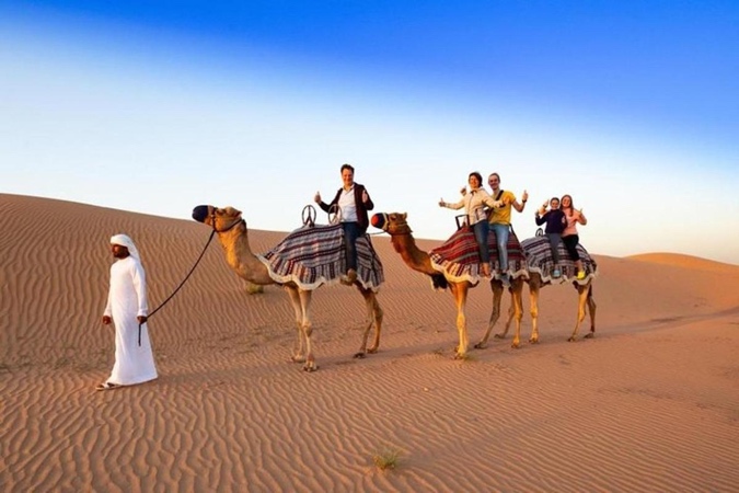 A group of people riding camels in the desert Description automatically generated