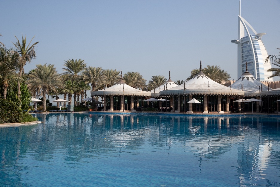A pool with a large building and palm trees

Description automatically generated