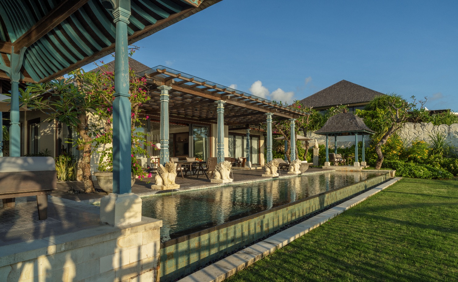 A pool with a gazebo and a building with a lawn and blue sky AI-generated content may be incorrect.